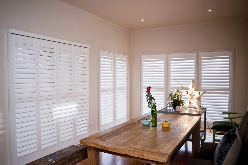 White plantation shutters installed around a dining area with a timber table