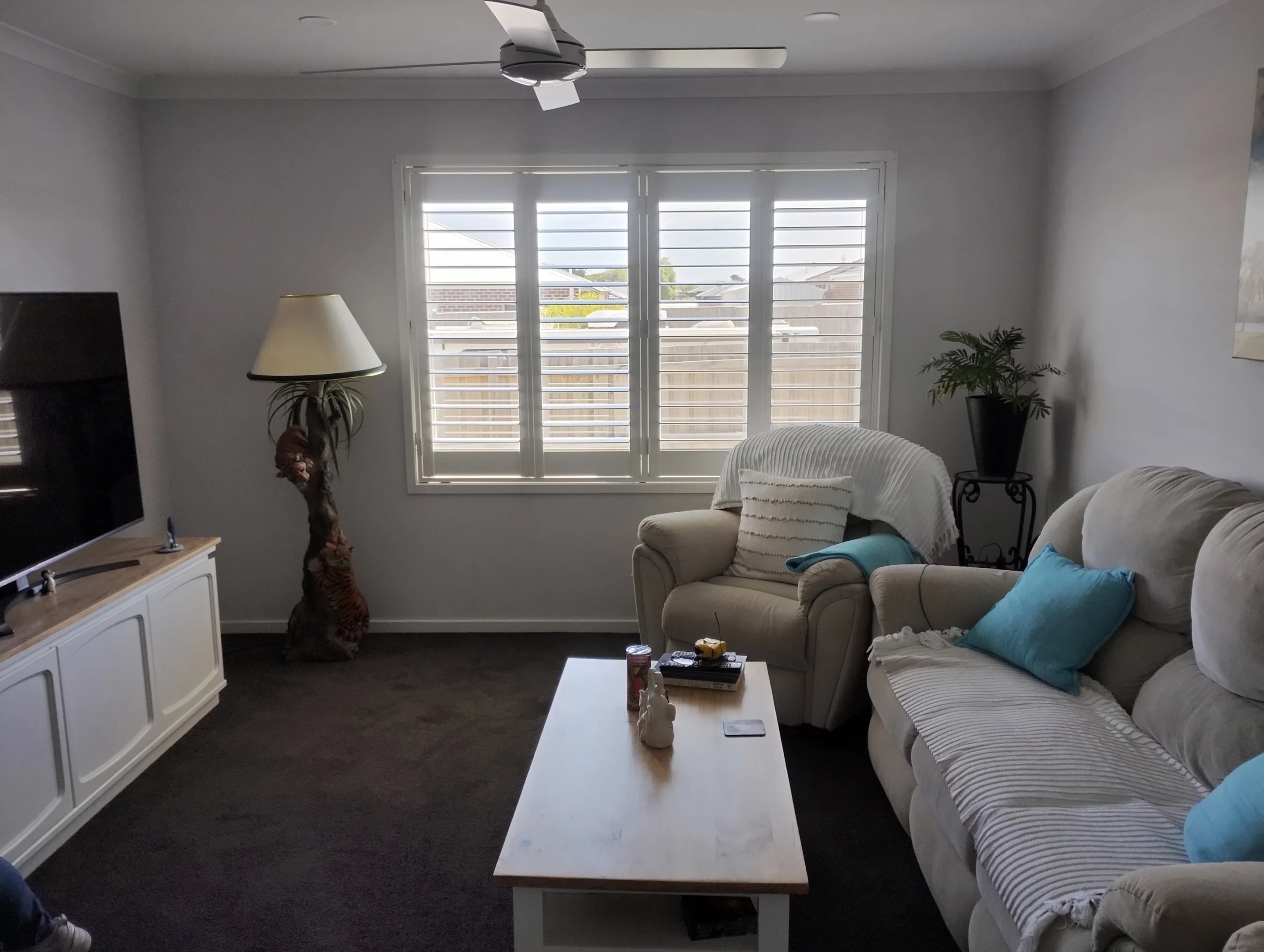 White plantation shutters across a lounge room window, with neighbouring homes visible beyond